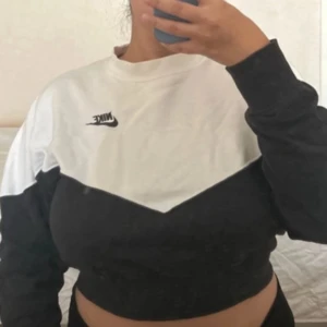 Svartvit croppad sweatshirt från Nike - Säljer en snygg croppad sweatshirt från Nike i svart och vitt. Tröjan har lång ärm, rund halsringning och en tydlig Nike-logga på bröstet. Perfekt för en sportig och avslappnad stil.
