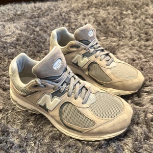 New Balance 2002r gråa - Säljer ett par gråa New Balance sneakers med grå detaljer andningsförmåga. Skorna har snörning och den klassiska N-loggan på sidan. Perfekta för dig som gillar stilrena och bekväma sneakers till vardags. Skorna är köpta för 1800kr på Vallgatan 12 i Göteborg och är i väldigt bra skick 👍