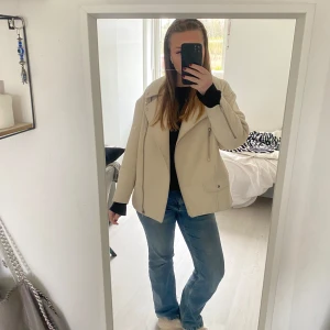 Beige bikerjacka med dragkedjor - Säljer en beige bikerjacka med silvriga dragkedjor och bred krage. Jackan har lång ärm och en snygg, lite oversized passform. Perfekt att slänga över en hoodie eller t-shirt för en cool look.