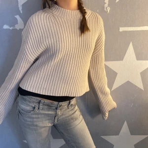 Beige ribbad croppad stickad tröja från H&M - Säljer en beige croppad stickad tröja från H&M med ribbad struktur. Tröjan har lång ärm och en avslappnad passform, perfekt för lager-på-lager. Enkel och stilren design som passar till mycket.