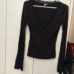 Svart långärmad topp med spets från Nelly - Säljer en svart långärmad topp från Nelly i storlek XXS. Toppen har djup v-ringning och spetsdetaljer längs halsringningen. Perfekt för att skapa en stilren och feminin look.♠️