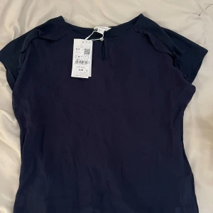 Mörkblå blus från Springfield - Säljer en stilren mörkblå blus från Springfield i storlek XS. Blusen har korta ärmar och en liten öppning med knapp vid halsen. 