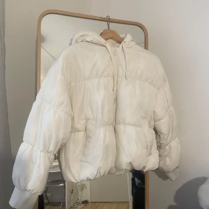 Vit pufferjacka med huva från H&M Divided - Säljer en fluffig vit pufferjacka från H&M Divided i storlek XS. Jackan har huva, dragkedja framtill och en oversized passform. Perfekt för kyliga dagar när du vill hålla dig varm och snygg.