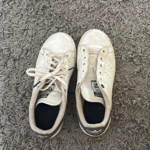 Vita Adidas Stan Smith sneakers - Klassiska vita Adidas Stan Smith sneakers med jeans detalj på hälen. Dock saknar ena skon snören men det är lätt att fixa 
