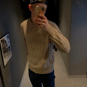 Beige stickad tröja från Bläck - Säljer en stilren beige stickad tröja från Bläck. Tröjan har ett klassiskt flätmönster och ärmar med ribbade muddar.