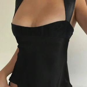 Svart satinlinnetopp från SHEIN - Säljare en svart linnetopp i satin från SHEIN. Toppen har breda axelband, fyrkantig urringning och knytband i ryggen. Snygg och stilren modell som ger en elegant look.