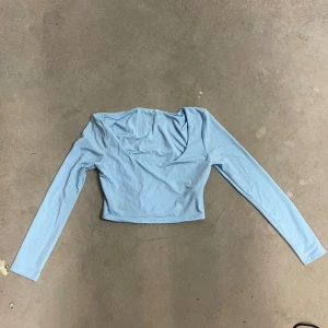 Ljusblå croppad långärmad topp från Shein - Säljer en ljusblå långärmad topp från Shein med croppad passform och v-ringad hals. Toppen är tillverkad i ett mjukt och stretchigt syntetmaterial, perfekt för en trendig vardagslook.