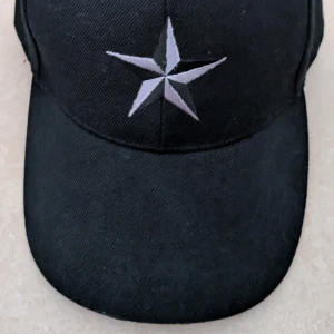Svart keps med broderad stjärna - Svart keps med en stor, broderad stjärna i silver och grått framtill. Klassisk böjd skärm och justerbar baksida. Perfekt för dig som vill ha en stilren och cool accessoar. Kepsen har aldrig använts 