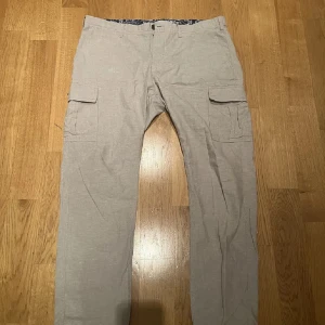 Beige cargolinnebyxor - Säljer ett par beige cargobyxor med stora sidofickor och bakfickor med knappar. Byxorna har rak passform och är perfekta för en avslappnad stil. Tillverkade i ett lätt och bekvämt material som passar till vardags. Storlek 38/32 men små i storleken så skulle säga att de passar de flesta som har runt L