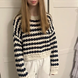 Randig stickad tröja i blått och vitt - Säljer en stickad tröja med breda blå och vita ränder. Tröjan har lång ärm och en lite croppad passform. Perfekt för dig som gillar en avslappnad men ändå trendig stil.