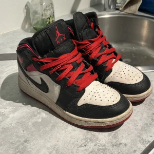 Nike Air Jordan med röda snören - Säljer ett par Nike Air Jordan med svart, vit och röd färgkombination. Skorna har röda snören, svart swoosh och perforerad vit tå. Klassisk Jordan-logga på plösen och låg modell. Perfekta för dig som gillar streetwear och sneakers. Unisex