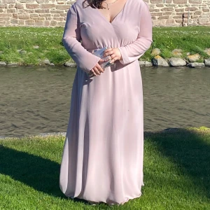 Ljusrosa balklänning med öppen rygg - Elegant ljusrosa långklänning med v-ringad hals och öppen rygg. (Svarta pricken på första bilden är ett bi, inte en fläck på klänningen). Klänningen har en markerad midja och ett flytande tyg. Perfekt för bal, bröllop eller andra speciella tillfällen. Den öppna ryggen har tillsytt spetstyg, se bild 5, och v-ringning är fastsydd. 💗Person på bild är 159cm och brukar ha storlek 48-50. Fler bilder och mått kan skickas vid efterfrågan. 