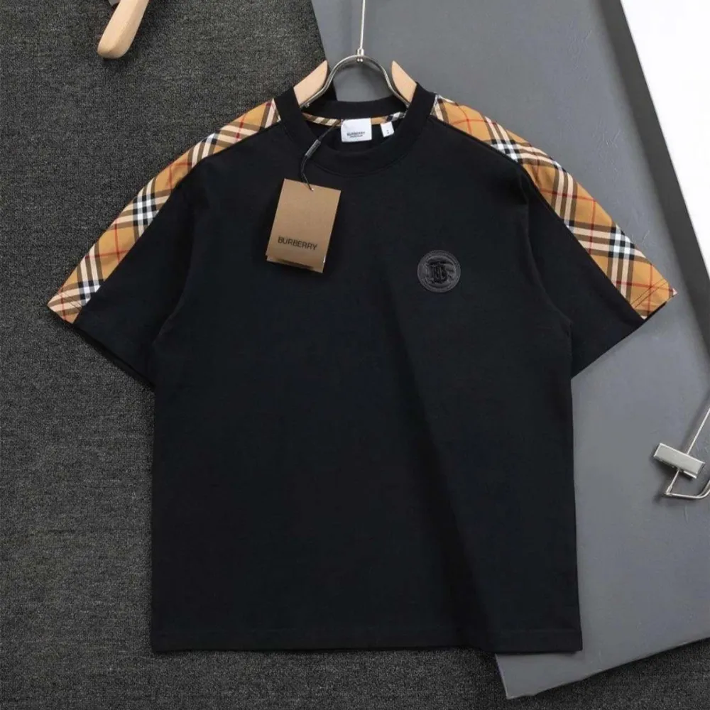 Svart t-shirt med klassiska Burberry-rutiga detaljer på ärmarna. Rund halsringning och diskret logga på bröstet. Perfekt för en stilren och trendig look.. T-paidat.