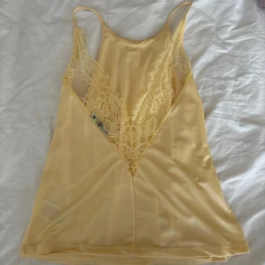 Gul linnetopp med spetsdetaljer - Snygg gul linnetopp med tunna axelband och v-ringning. Toppen har fina spetsdetaljer framtill samt baktill 