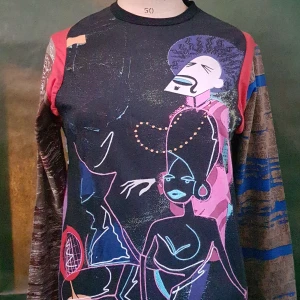 Färgstark långärmad tröja med grafiskt tryck - Unik långärmad tröja med färgglada grafiska motiv framtill och texten 'We have forgotten the truth' på ryggen. Tröjan har olika mönster och färger på ärmarna, bland annat blått, rött och brunt. Perfekt för dig som vill sticka ut.