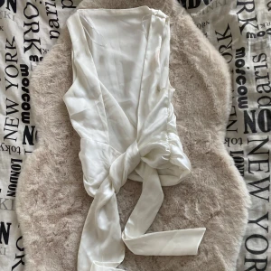Vit topp med öppen rygg  - Säljer en vit topp med öppen rygg. Perfekt för att skapa en elegant look. Toppen har en enkel design som gör den lätt att matcha med olika outfits. Toppen är använd en gång.