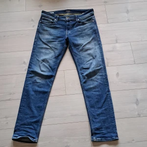 Blå jeans från Jack & Jones - Snygga blå jeans från Jack & Jones med en klassisk femficksdesign. De har en knappgylf och subtila slitningar för en trendig look. Perfekta för en avslappnad stil.