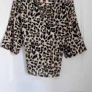 Leopardmönstrad topp från Flash Woman - Snygg leopardmönstrad topp från Flash Woman med trekvartsärmar och snörning framtill. Perfekt för att ge en djärv touch till din outfit. 🐆
