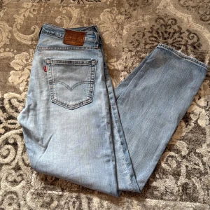 Ljusa jeans från Levi's - Säljer ett par ljusa jeans från Levi's med klassisk femficksdesign och en snygg läderpatch baktill. Jeansen har en rak passform och är perfekta för en avslappnad stil. De är tillverkade i slitstarkt denim och har en ikonisk röd etikett vid bakfickan. Och är använd få par gånger 