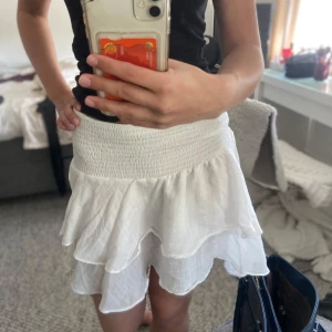 Vit volangkjol - Säljer en söt vit kortkjol med volanger. Kjolen har en elastisk midja som ger en bekväm passform. Perfekt för varma sommardagar! Aldrig använd ❤️