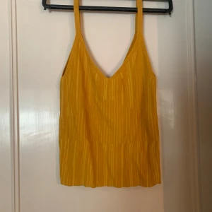 Gul ribbad linnetopp från H&M - Säljer en solgul ribbad linnetopp från H&M. Toppen har smala axelband och en v-ringad design som ger en somrig känsla. Perfekt för varma dagar!