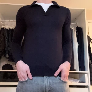 Riley Merino Tröja - Snygg svart tröja från Riley i mjuk merinoull. Tröjan har en klassisk krage och långa ärmar, perfekt för en stilren look. Passar bra till både jeans och chinos👌🏽