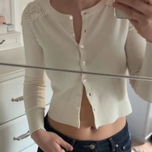 Vit kofta med spetsdetaljer - Säljer en stilren vit kofta med vackra spetsdetaljer på axlarna. Köpt secondhand men aldrig använd. Har inga deffekter💓