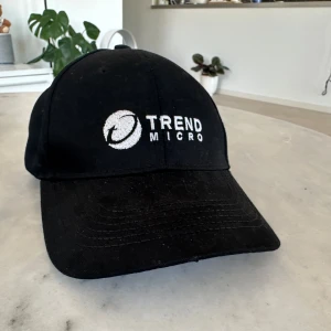 Svart keps med broderad logotyp - Snygg svart keps med justerbar rem och broderad vit logotyp från Trend Micro. Perfekt för en casual look.