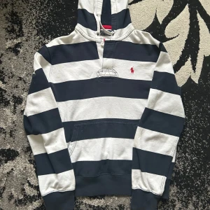  Polo Ralph Lauren Hoodie - Säljer en snygg randig hoodie från Polo Ralph Lauren i svart och vit. Tröjan har en klassisk känguruficka och en broderad röd logga på bröstet. Perfekt för en avslappnad stil.