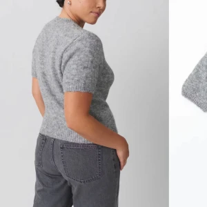 Grå stickad tröja från Gina  - Säljer en mysig grå stickad tröja från Gina. Tröjan har korta ärmar och en rund halsringning, perfekt för lager-på-lager under kyligare dagar. Den är tillverkad i ett mjukt material som ger en skön känsla mot huden.