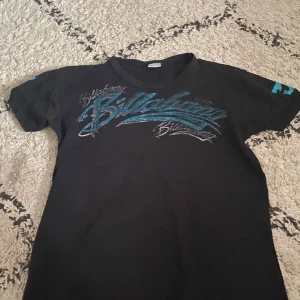 Svart t-shirt från Billabong - Snygg svart t-shirt från Billabong med blått tryck på både fram- och baksidan. Perfekt för en avslappnad stil. Kortärmad och tillverkad i ett bekvämt material.
