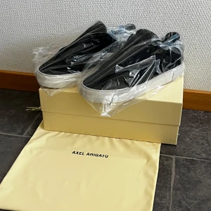 Svarta sneakers från Axel Arigato - Snygga svarta sneakers från Axel Arigato med vit sula. Perfekta för en stilren look. Skorna kommer i originalförpackning med en praktisk dustbag.
