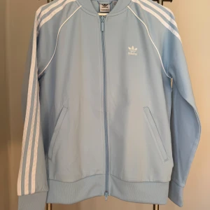 Ny, oanvänd, ljusblå jacka från Adidas med prislappen kvar! - Ny, oanvänd, ljusblå jacka från Adidas i storlek M med prislappen kvar.  Nypris ca 599kr