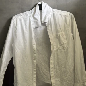 Vit skjorta från Kappahl - Säljer en klassisk vit skjorta från Kappahl i storlek 164. Skjortan har en bröstficka och långa ärmar, perfekt för en stilren look. Tillverkad i ett lätt och bekvämt material.