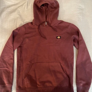 Brun hoodie från Dickies - Säljer en snygg brun hoodie från Dickies i storlek medium. Tröjan har en klassisk känguruficka och en justerbar huva med dragsko. Perfekt för en avslappnad stil.