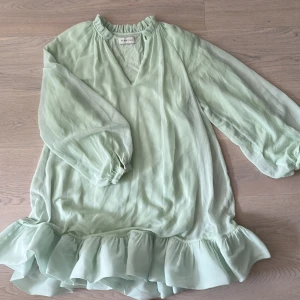 Mintgrön klänning från By Malina - Säljer en mintgrön klänning från By Malina med volangdetaljer vid fållen. Klänningen har långa ärmar och en v-ringad hals. Perfekt för en somrig look! 🌿