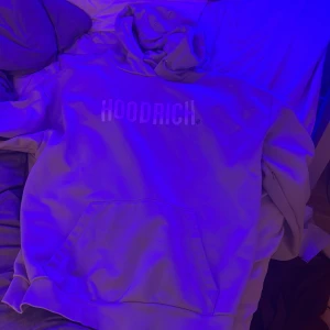Grå hoodie från Hoodrich - Säljer en snygg beige hoodie från Hoodrich med tryck på bröstet och ärmen. Den har en klassisk känguruficka och en bekväm huva. Perfekt för en avslappnad stil. Endast använd ett fåtal gånger (pris kan diskuteras)