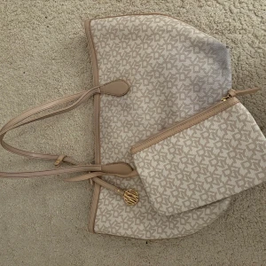 Beige mönstrad axelväska från DKNY - Snygg beige axelväska från DKNY med matchande liten plånbok/väska på sidan. Den är i fint sick och modellen säljs ej längre