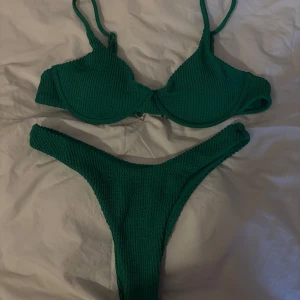 Grön ribbad bikini - OANVÄND! Snygg grön bikini med ribbad textur. Överdelen har justerbara axelband och en bygel för extra stöd. Underdelen är i en klassisk tanga-model.