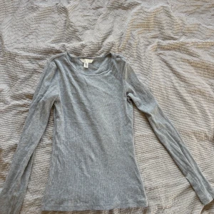 Grå ribbad långärmad topp - Säljer en stilren grå ribbad topp med långa ärmar. Perfekt för lager-på-lager eller som den är. Enkel och mångsidig design som passar till det mesta. Hör av dig vid intresse!