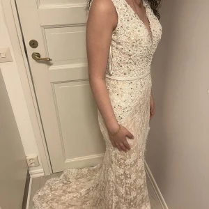 Vit spetsklänning med öppen rygg - Elegant vit långklänning i spets med v-ringning och öppen rygg. Klänningen har en smickrande passform och ett vackert släp. Perfekt för speciella tillfällen.Pris diskuteras vid snabb affär,passar dig för 34 och 36 