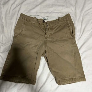 Beige shorts med knappar - Snygga beige shorts med knapp och dragkedja framtill. De har en klassisk design med fickor både fram och bak, vilket gör dem praktiska och stilrena. Perfekta för en avslappnad look.