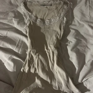 Beige ribbad linne från RoseBud - Säljer en söt beige ribbad linne från RoseBud med spetsdetaljer vid halsringningen. Linnet är ärmlös och har en smickrande passform. Perfekt för en stilren och bekväm look. 💕🤭