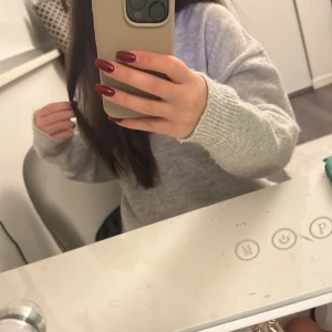 Grå stickad tröja från Gina Tricot - Mysig grå stickad tröja från Gina Tricot. Perfekt för kyliga dagar med sin mjuka och bekväma passform. Tröjan har långa ärmar och ribbade muddar vid ärmslut och nederkant. Ett måste i garderoben för en stilren look.