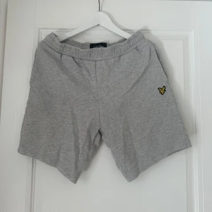 Grå shorts från Lyle & Scott - Säljer ett par grå shorts från Lyle & Scott med elastisk midja och en liten broderad logga på framsidan. Shortsen har en bakficka och är perfekta för en avslappnad stil.