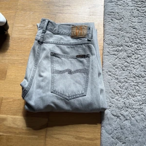 Grå jeans från Nudie Jeans - Snygga grå jeans från Nudie Jeans med klassisk femficksdesign. Byxorna är tillverkade i slitstarkt denim. Perfekta för en stilren vardagslook. Modell: Tuff Tony Färg: Mountain grey