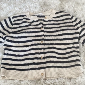 Randig kofta från Gina Tricot - Säljer en snygg randig kofta från Gina Tricot i svart och beige. Koftan har långa ärmar och knappar framtill. Perfekt för en stilren look.⭐️