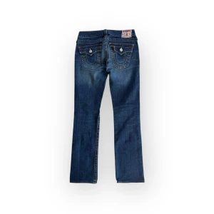 True Religion Billy jeans - Snygga mörkblå raka/bootcut jeans med broderad hästsko på bakfickorna och en klassisk femficksdesign. Längd 103, innerbenet 75, midja 38, benöppning 18. Storlek W27, passar S.  Inga tydliga defekter