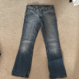 Blå bootcut jeans - Säljer ett par klassiska blå bootcut jeans med en lätt tvättad look. De har fem fickor och stängs med dragkedja och knapp. Perfekta för en avslappnad stil.