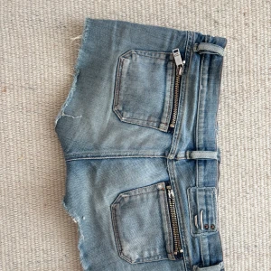 Blå jeansshorts med dragkedja - Säljer ett par coola blå jeansshorts med slitna detaljer och dragkedjor på fickorna ifrån märket diesel. Shortsen har en lågmidjad passform och bälteshällor för extra stil. Perfekta för en avslappnad look!